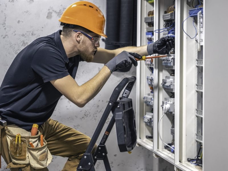 Young adult electrician civil engineer screwing equipment into fuse box. Young adult electrician civil engineer screwing equipment into fuse box.